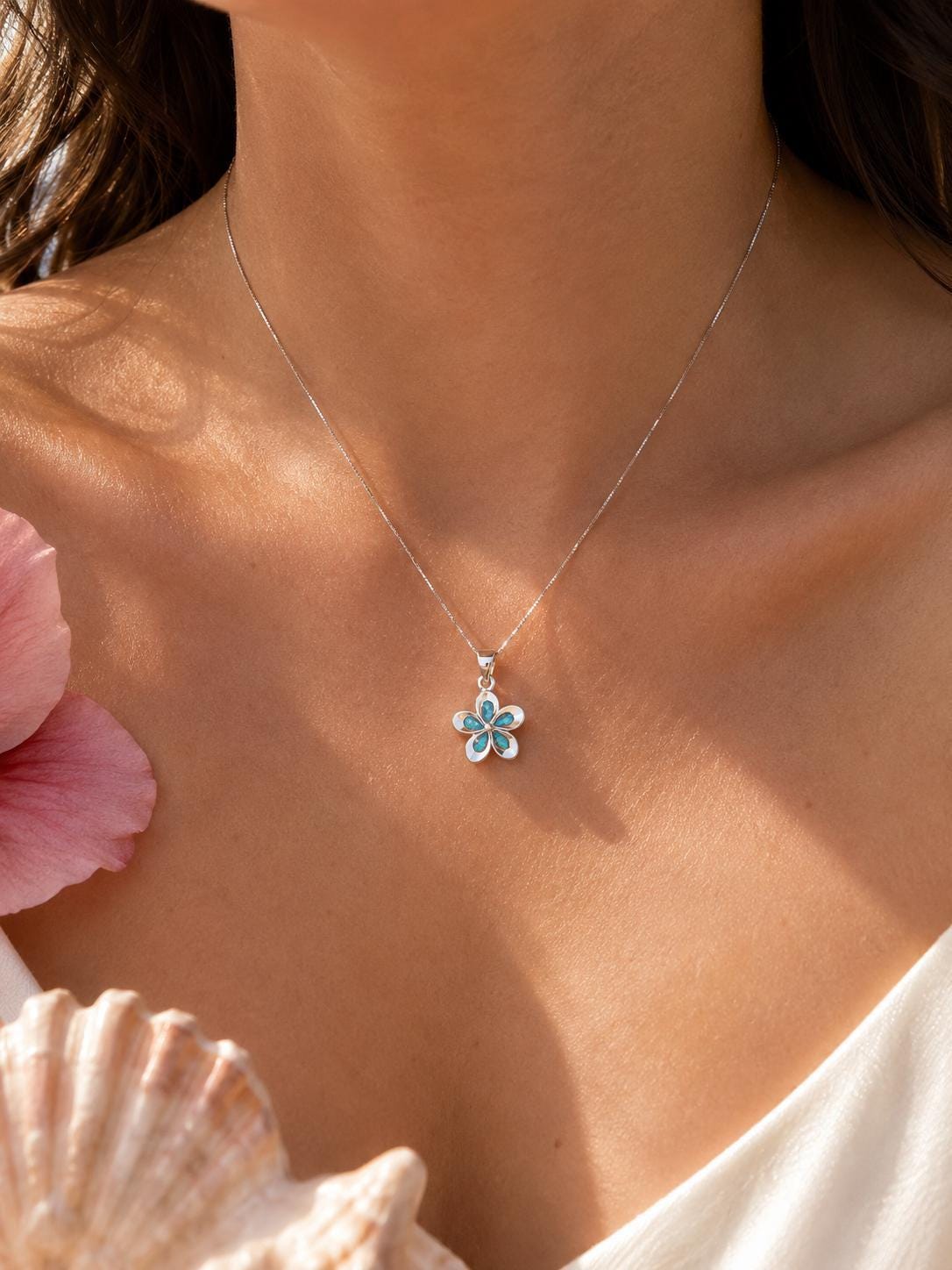 May include: A silver necklace featuring a delicate flower-shaped pendant. The pendant has five petals, each inlaid with a bright turquoise blue stone, suspended from a thin, polished silver chain that rests against the collarbone area.