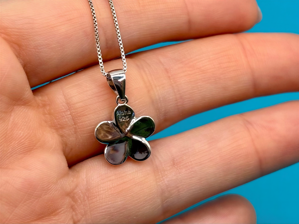 A silver flower pendant necklace is being held in a hand against a blue background.