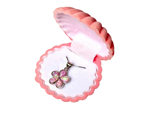A pink shell-shaped jewelry box containing a necklace with a flower pendant.