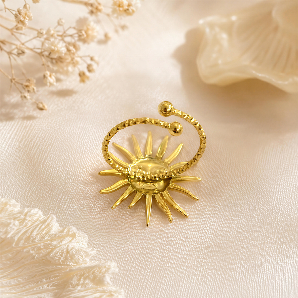 a gold ring with a sun-shaped design, placed on a white fabric surface.