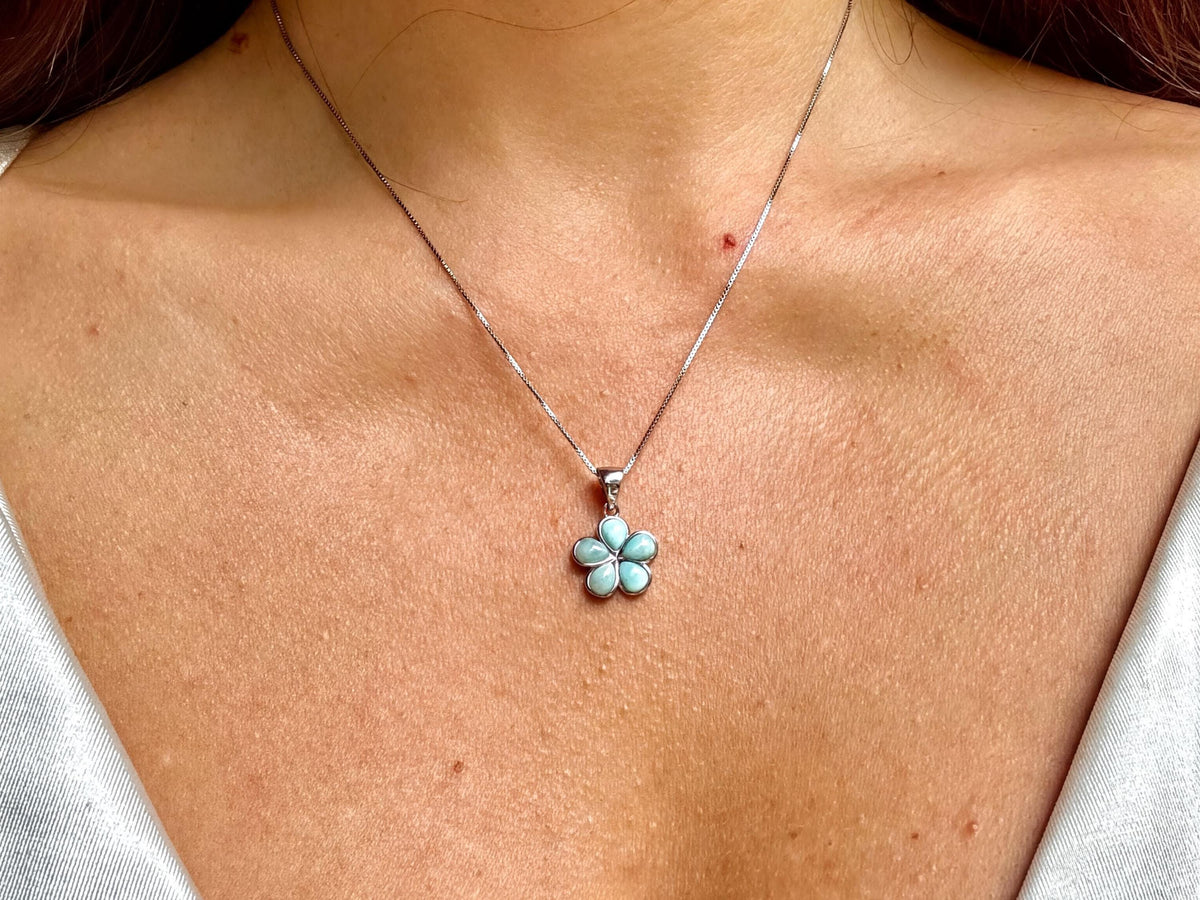 A close-up view of a woman's neck and chest area, showing a delicate necklace with a small flower pendant.
