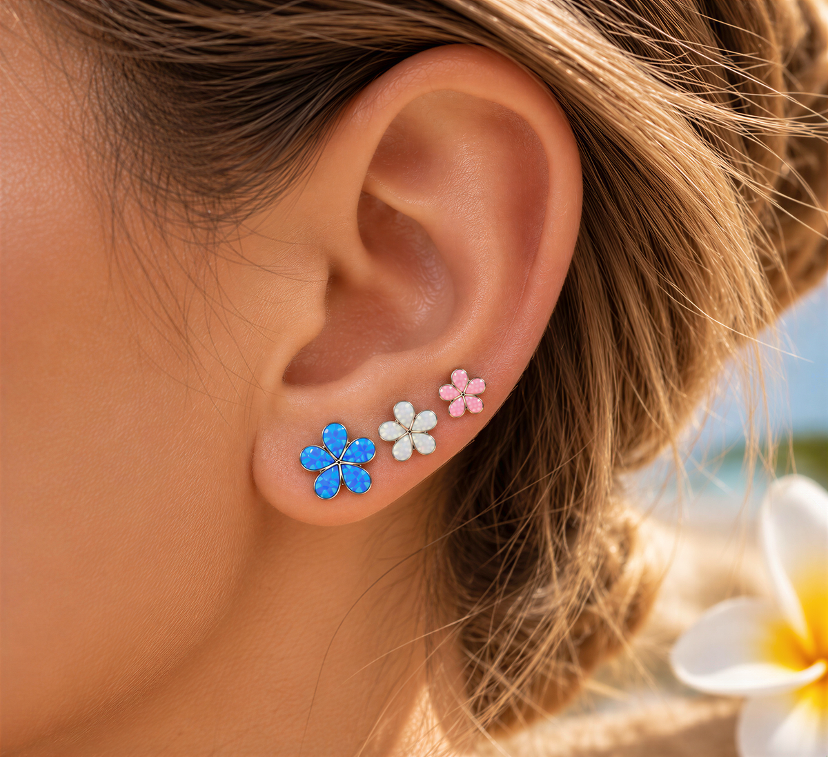 A close-up of a person's ear adorned with three flower-shaped earrings in blue, white, and pink colors.