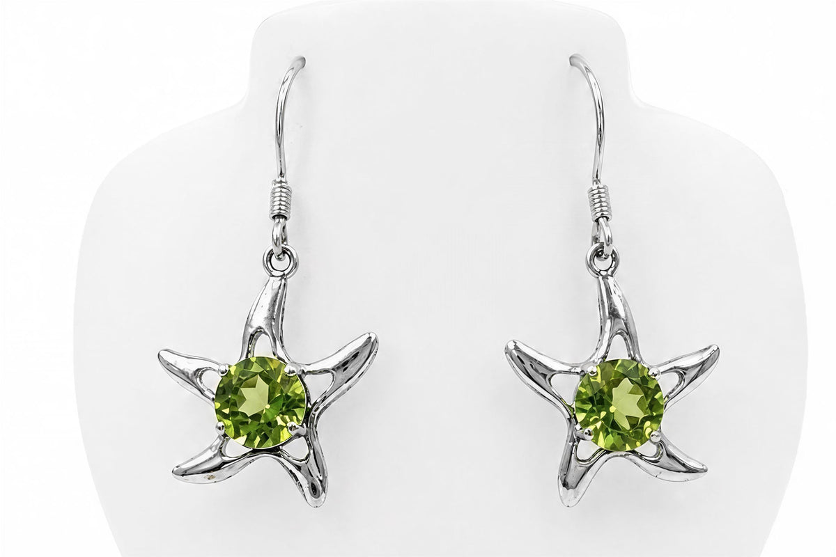A pair of silver earrings with green gemstones, shaped like stars, hanging from hooks.
