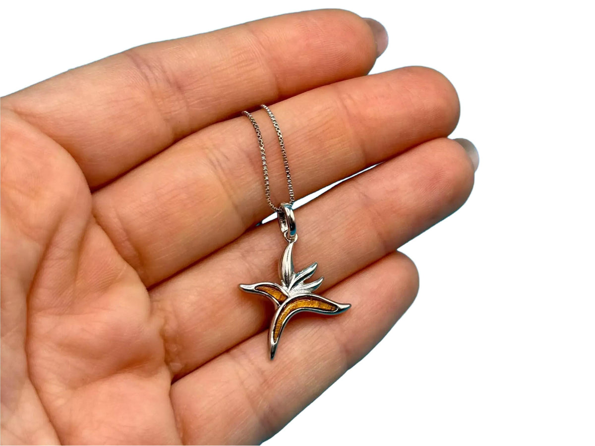 A hand holding a silver pendant with a flower design.