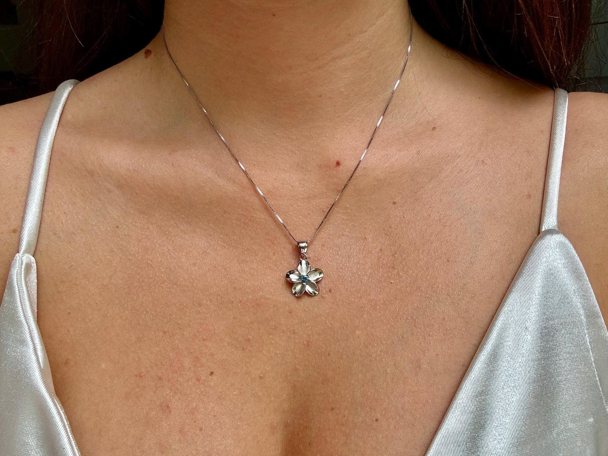 A close-up view of a woman's neck and chest area, showing a delicate silver necklace with a small pendant featuring a flower design.