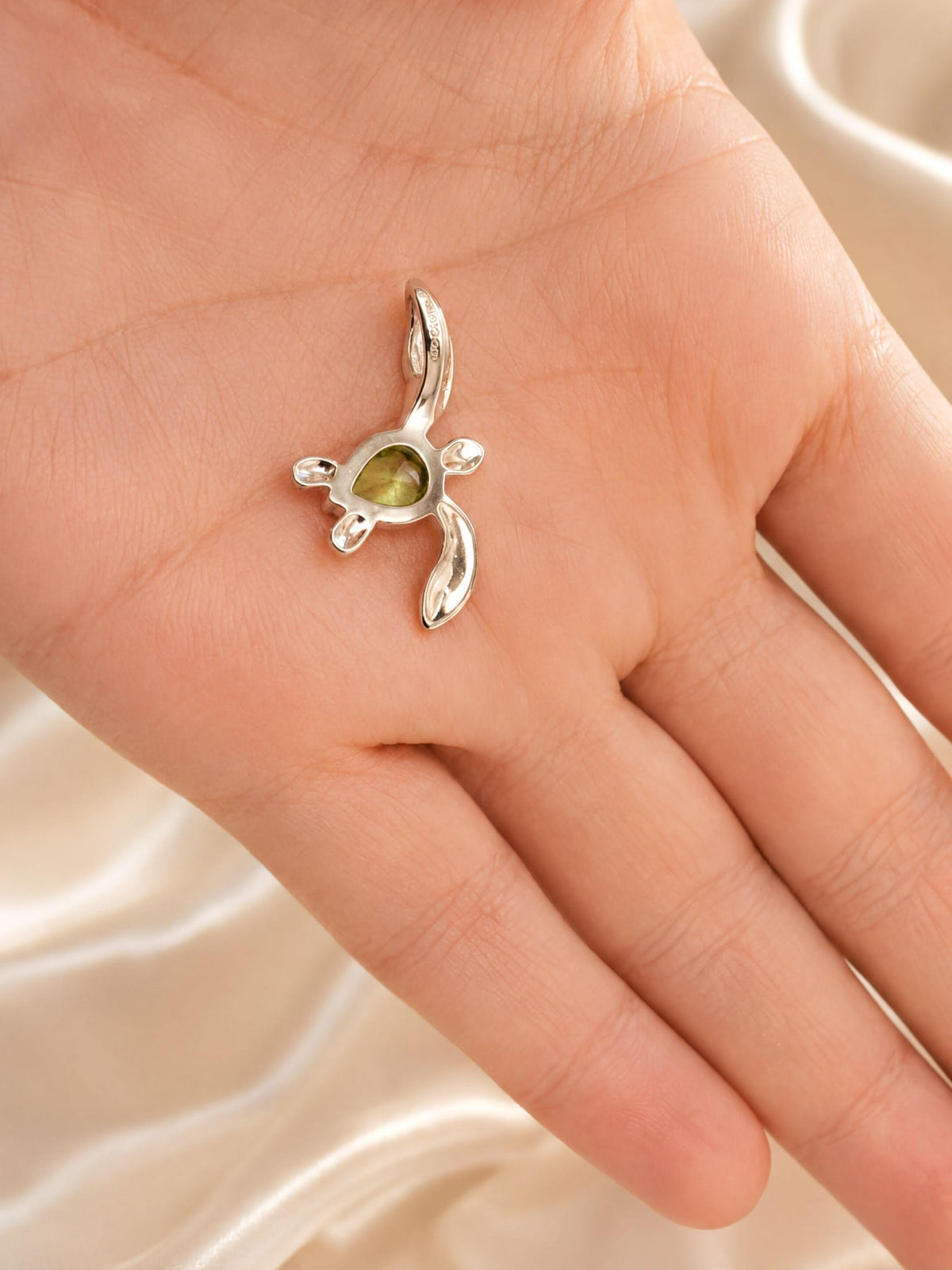A hand holding a small silver pendant in the shape of a turtle.