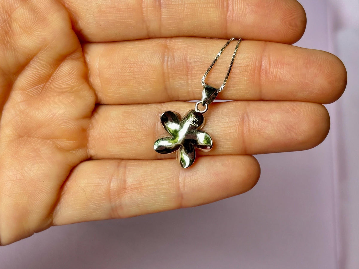 A hand holding a silver flower pendant necklace.