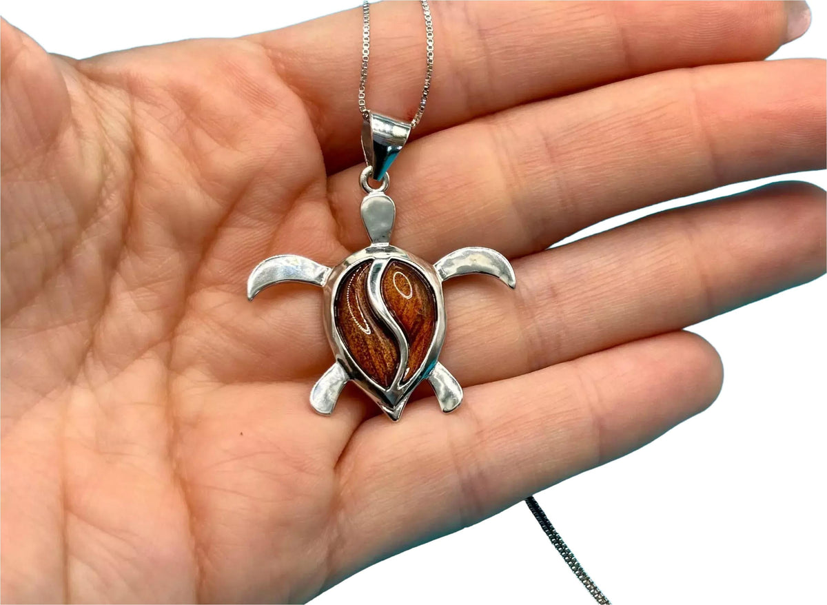 A hand holding a silver necklace with a pendant featuring a turtle design.