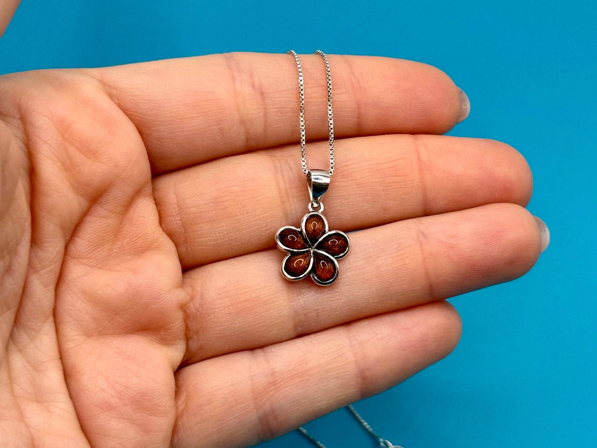 A hand holding a silver necklace with a pendant featuring a flower design.