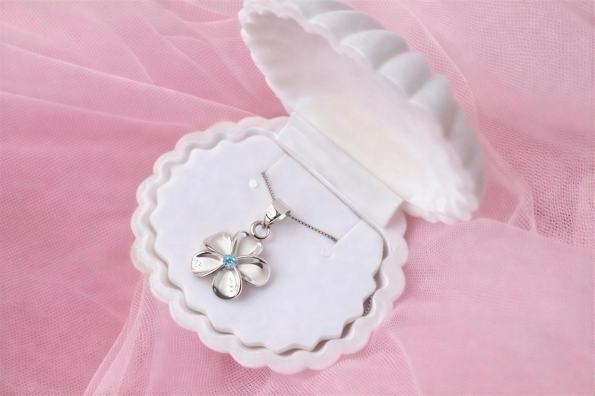 A white jewelry box containing a silver necklace with a blue gemstone pendant, placed on a pink background.