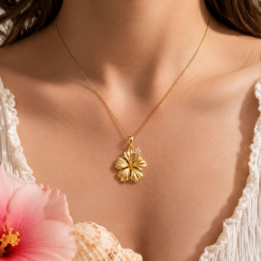 A close-up of a woman's neck and chest wearing a gold necklace with a large, intricately designed flower pendant. Hibiscus necklace