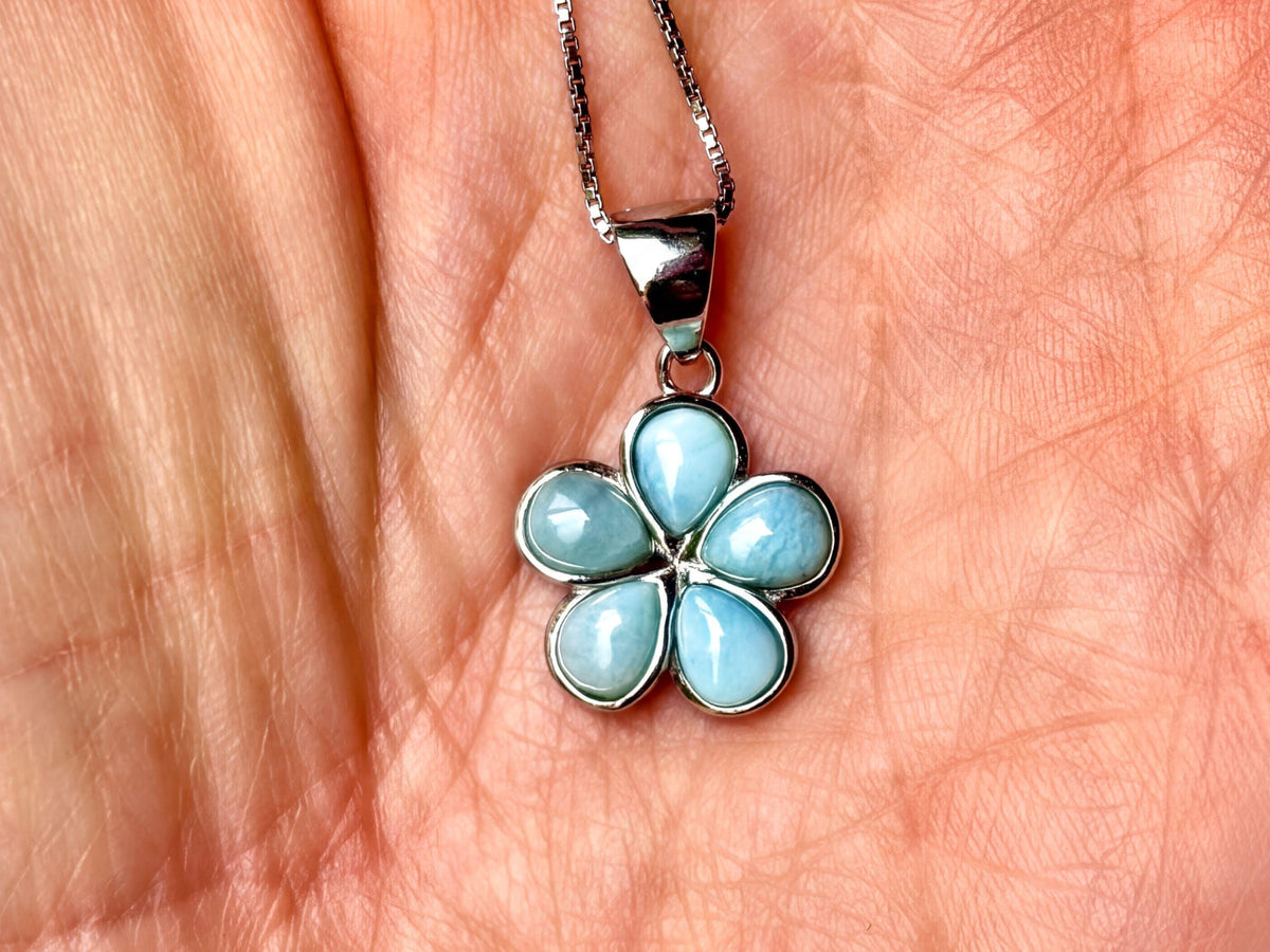 A silver flower-shaped pendant with blue gemstones is being held in a person's hand.