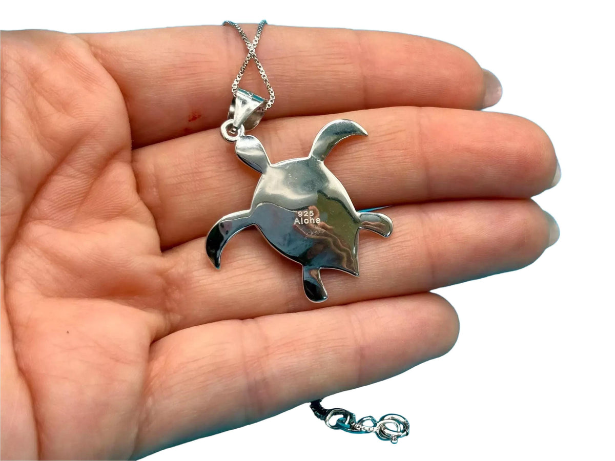 A silver necklace with a pendant in the shape of a turtle is being held in a person's hand.