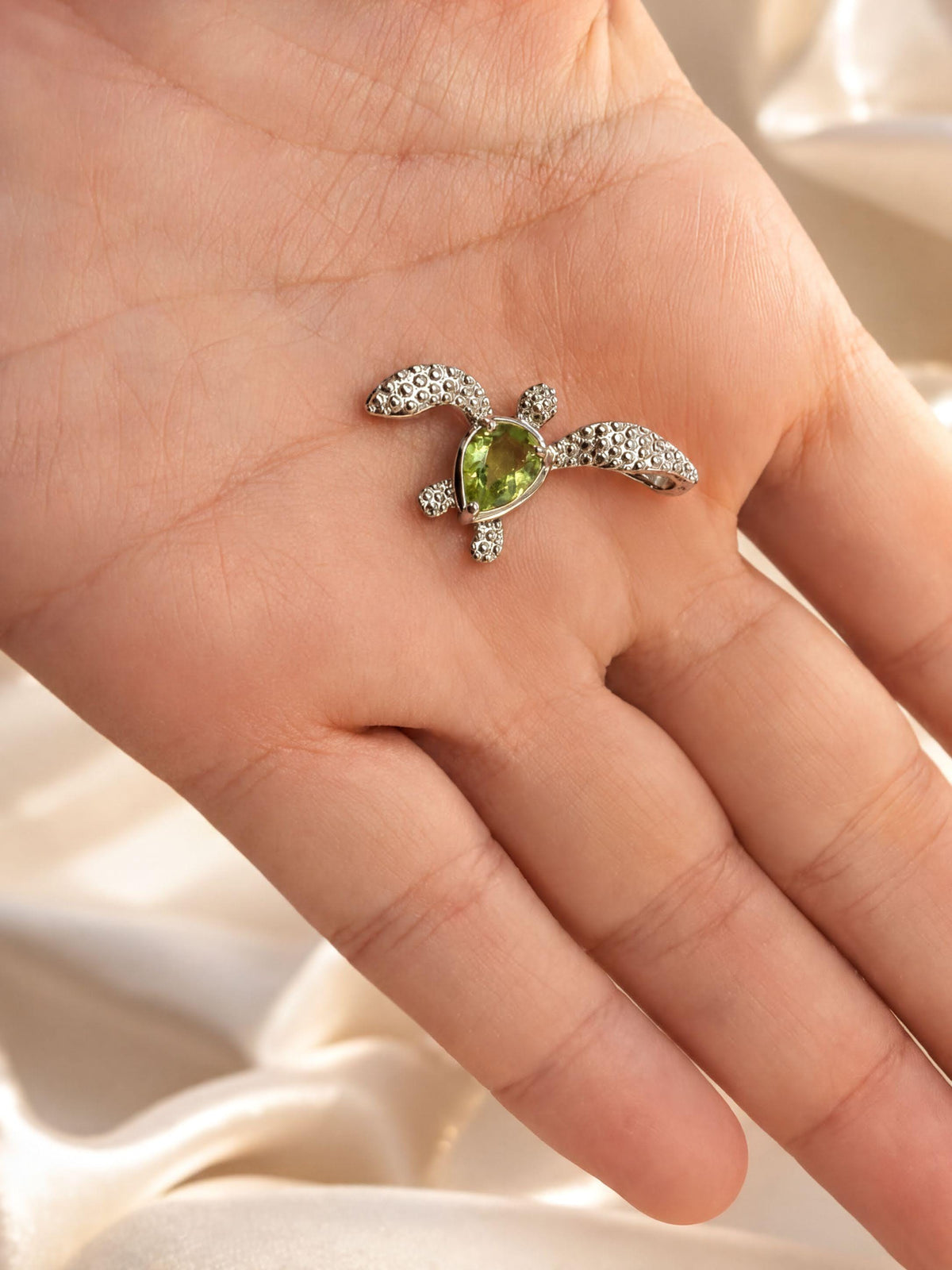 A hand holding a small, intricately designed necklace with a green gemstone.