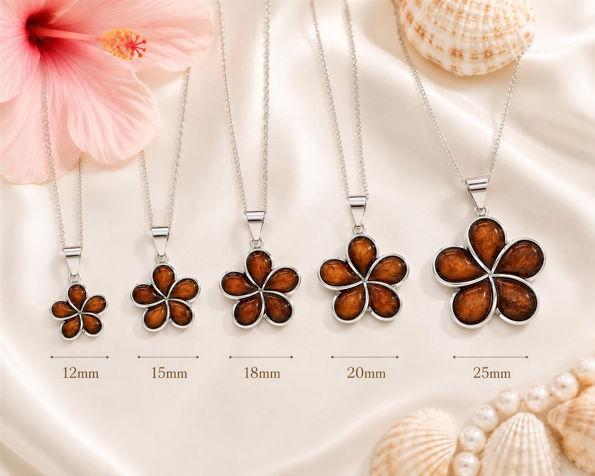 A collection of five pendant necklaces with different flower designs, each varying in size. The necklaces are displayed on a white background, with a pink hibiscus flower and seashells in the background.