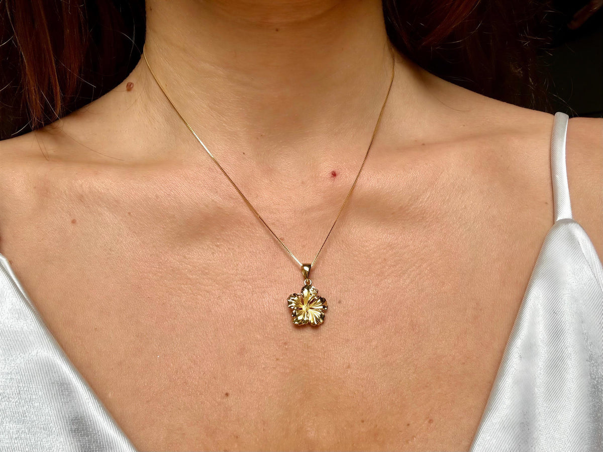 A close-up of a woman wearing a gold necklace with a pendant featuring a flower design.