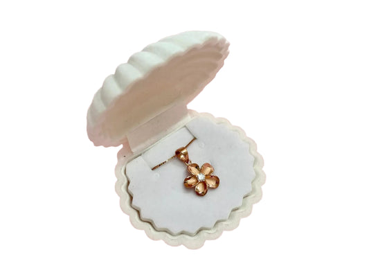 A white pendant necklace with a gold flower pendant is displayed in a white shell-shaped jewelry box.