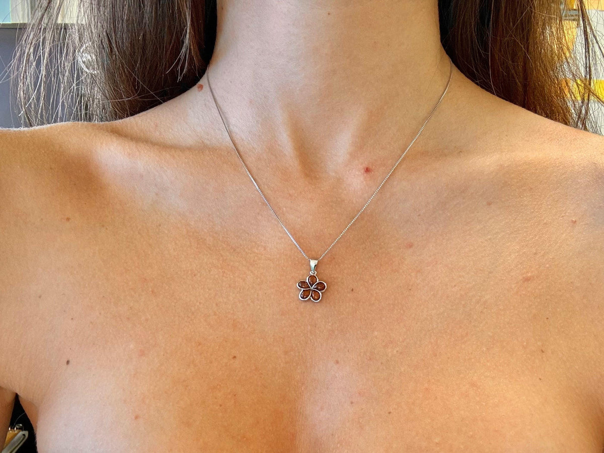 A close-up view of a woman's neck and chest area, showing a delicate silver necklace with a small flower pendant.