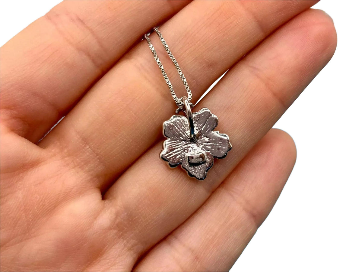 A hand holding a small silver flower-shaped pendant necklace.