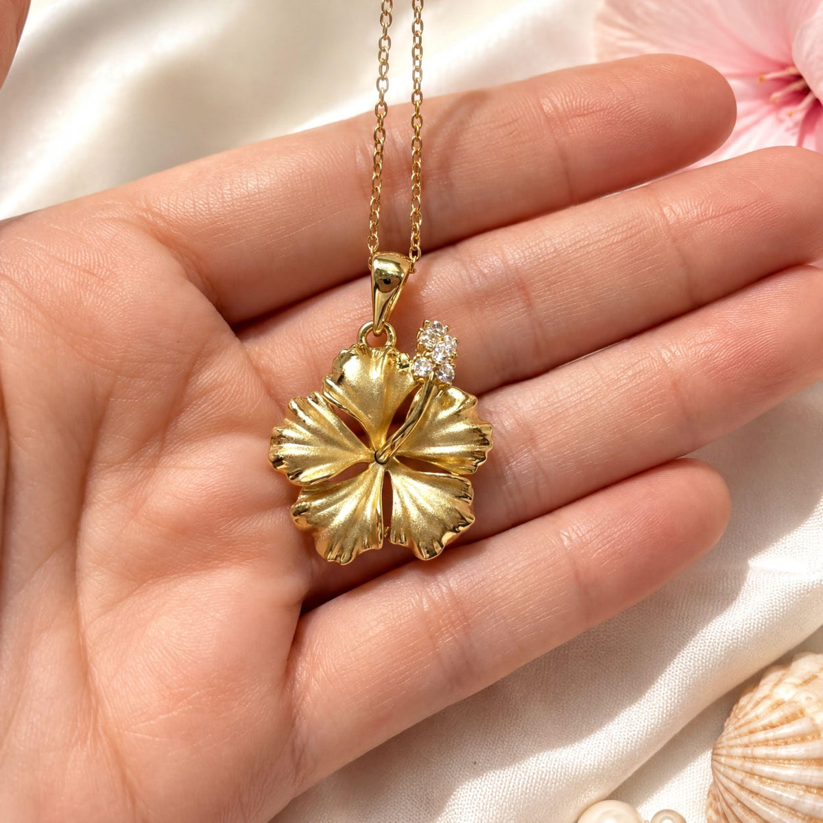 A hand holding a gold necklace with a large, intricately designed flower pendant.
