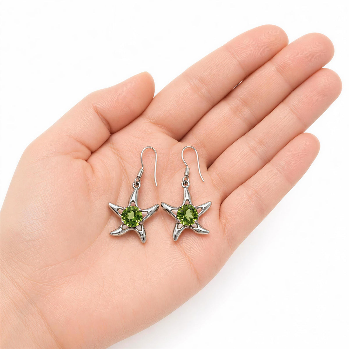 A hand holding a pair of silver earrings with green gemstones.